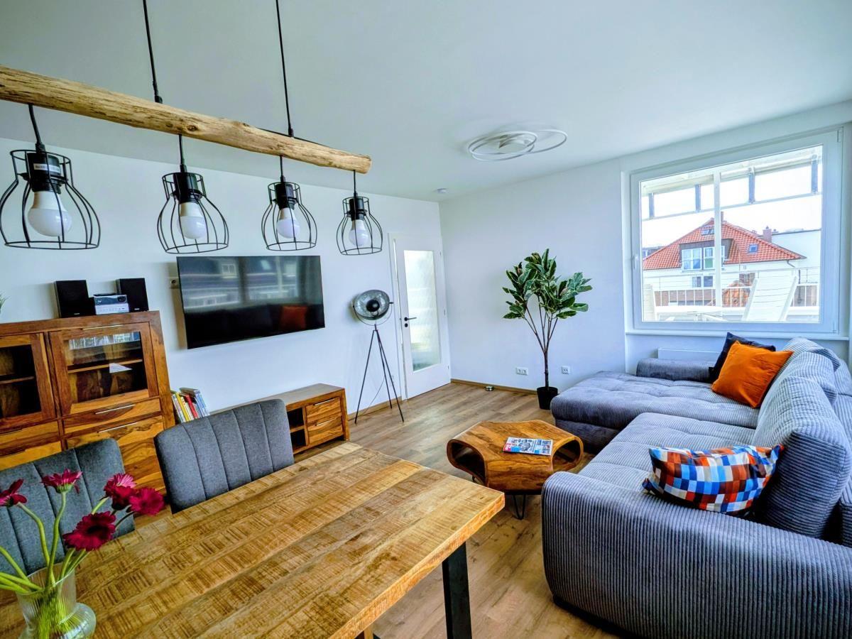 Wohn- und Essbereich mit Sofa, Tisch und Fernseher. Holzfußboden und große Fenster.