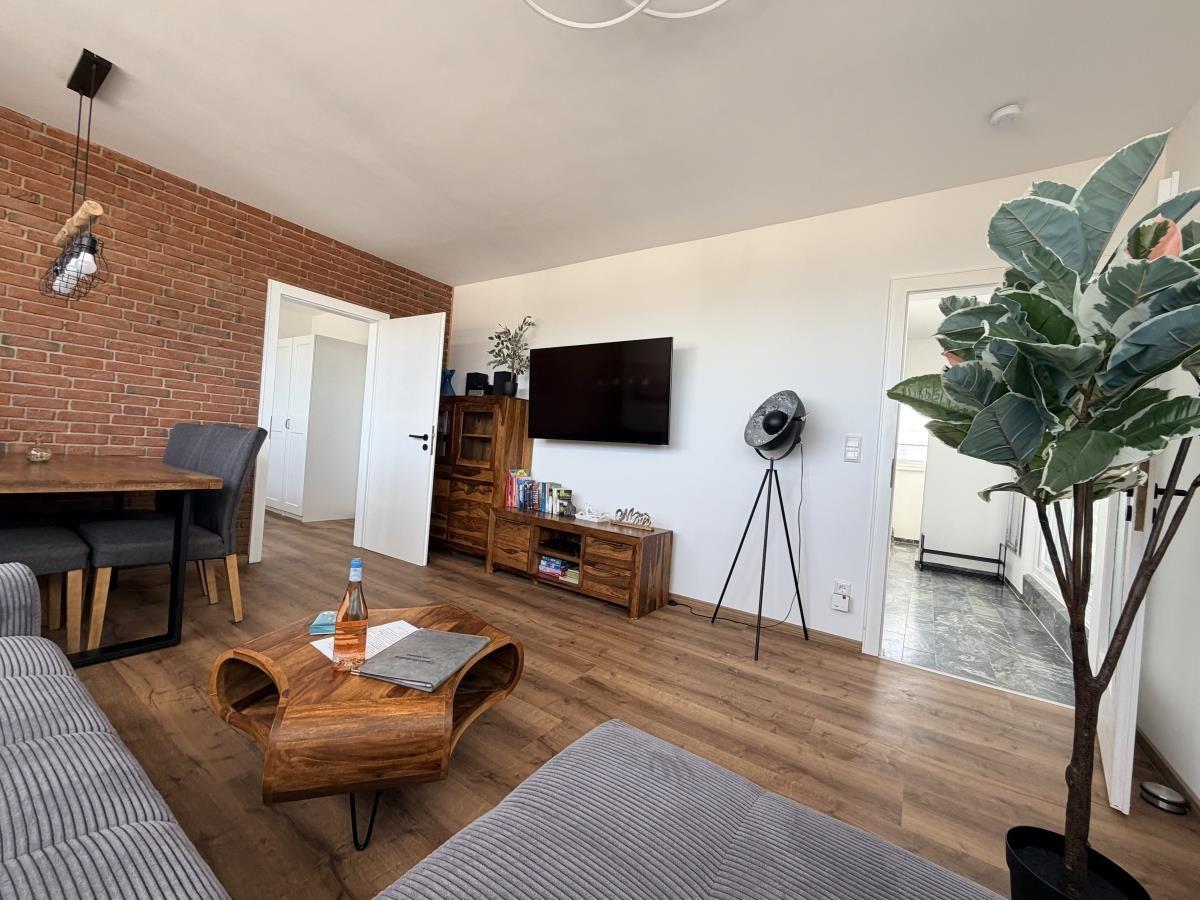 Wohnzimmer mit Holzboden, Fernseher, Couch und Essbereich mit Backsteinwand.