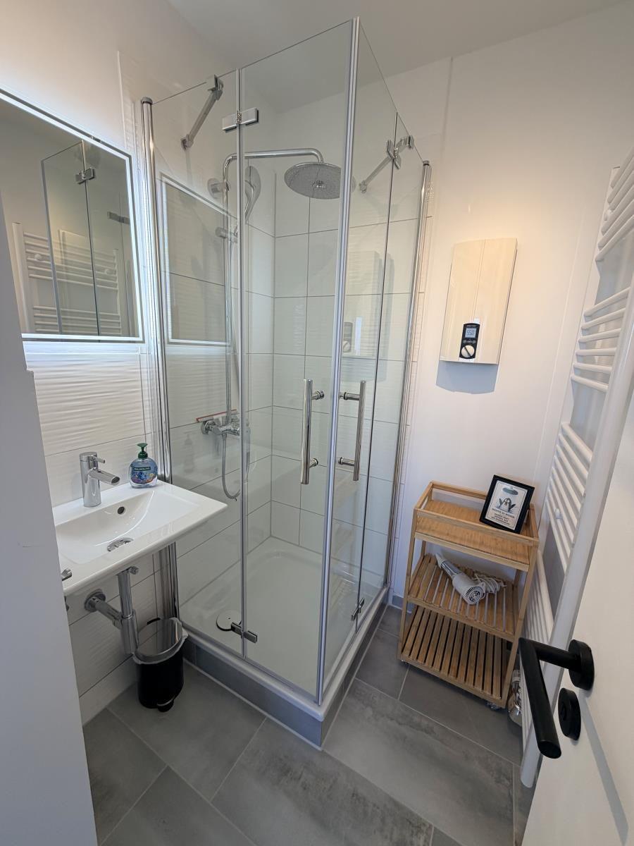 Badezimmer mit Dusche, Waschbecken und Handtuchwärmer.