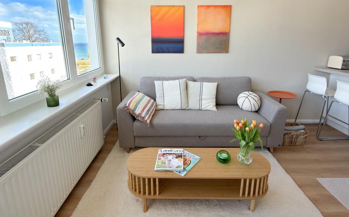 Ein Wohnzimmer mit grauem Sofa, Holztisch und Blick aufs Meer.