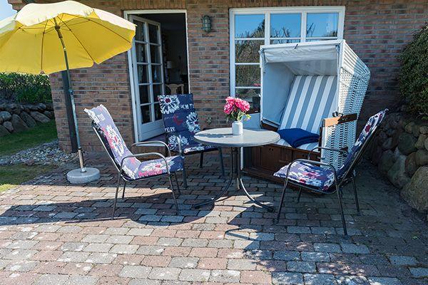Terrasse mit gelbem Sonnenschirm, Gartenstühlen und Tisch vor Backsteinhaus.