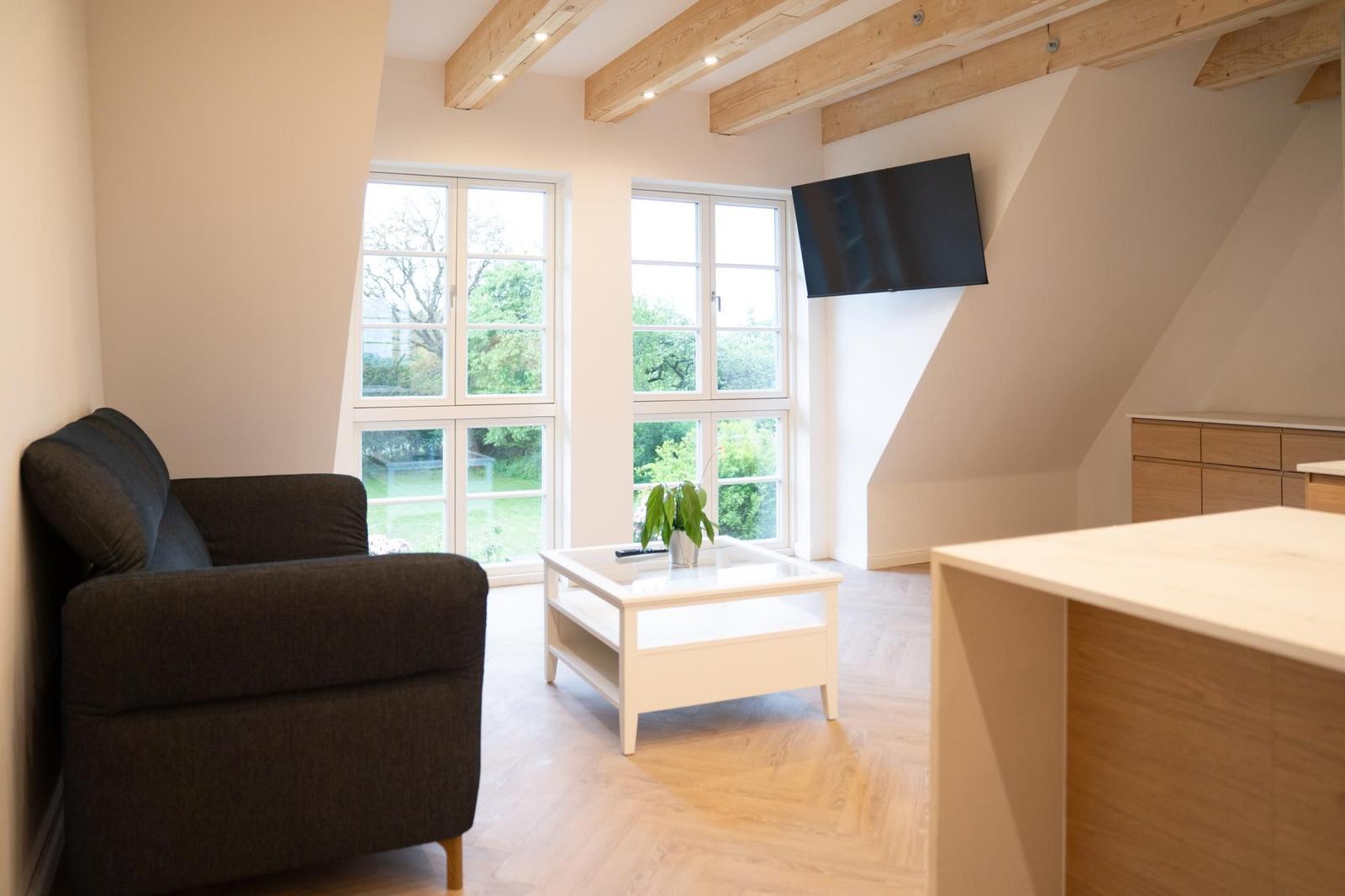 Wohnraum mit Sofa, TV und Fenstern zum Garten