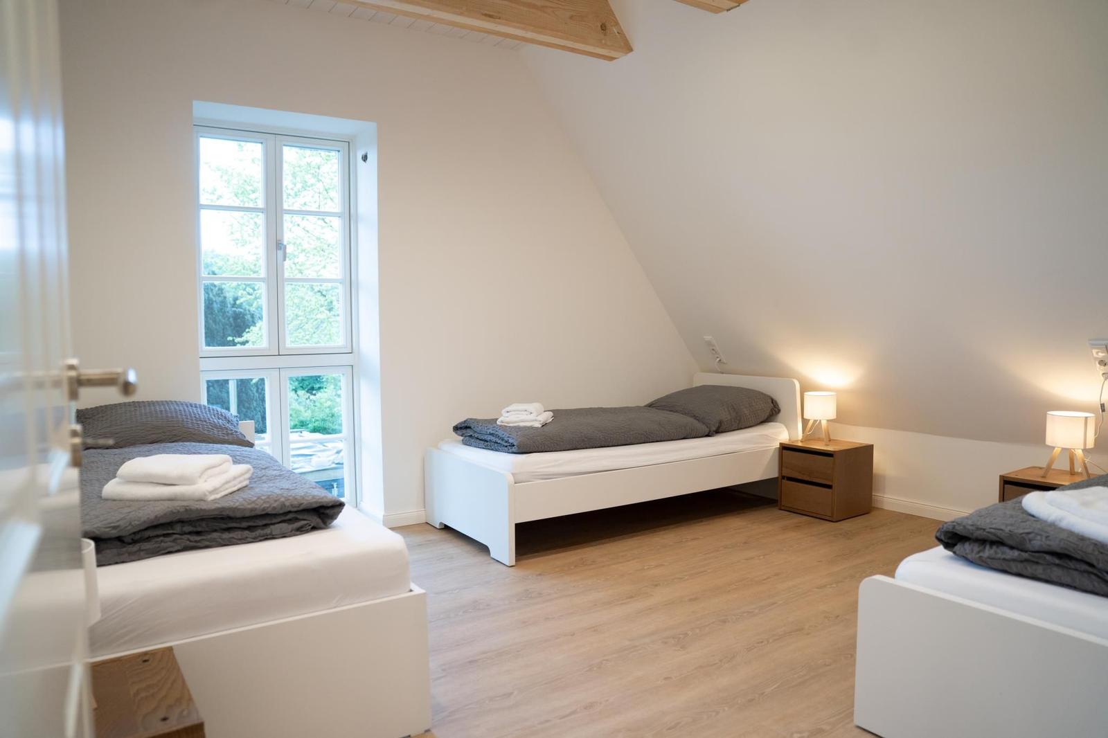 Drei Betten mit Bettwäsche, Holzboden und Fenster mit Blick nach draußen.