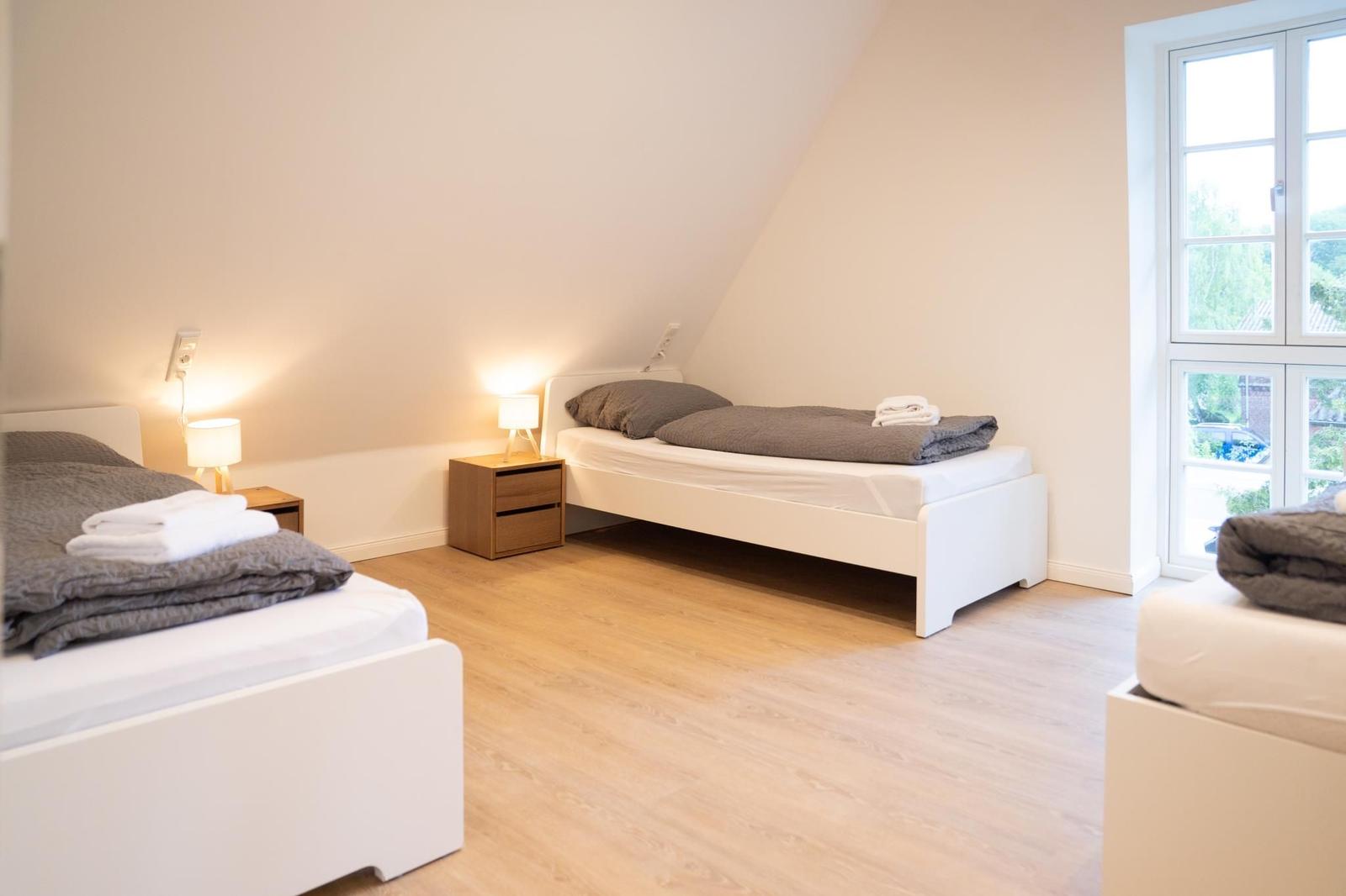 Zwei Betten mit grauen Bettwäschen und Nachttischen mit Lampen.