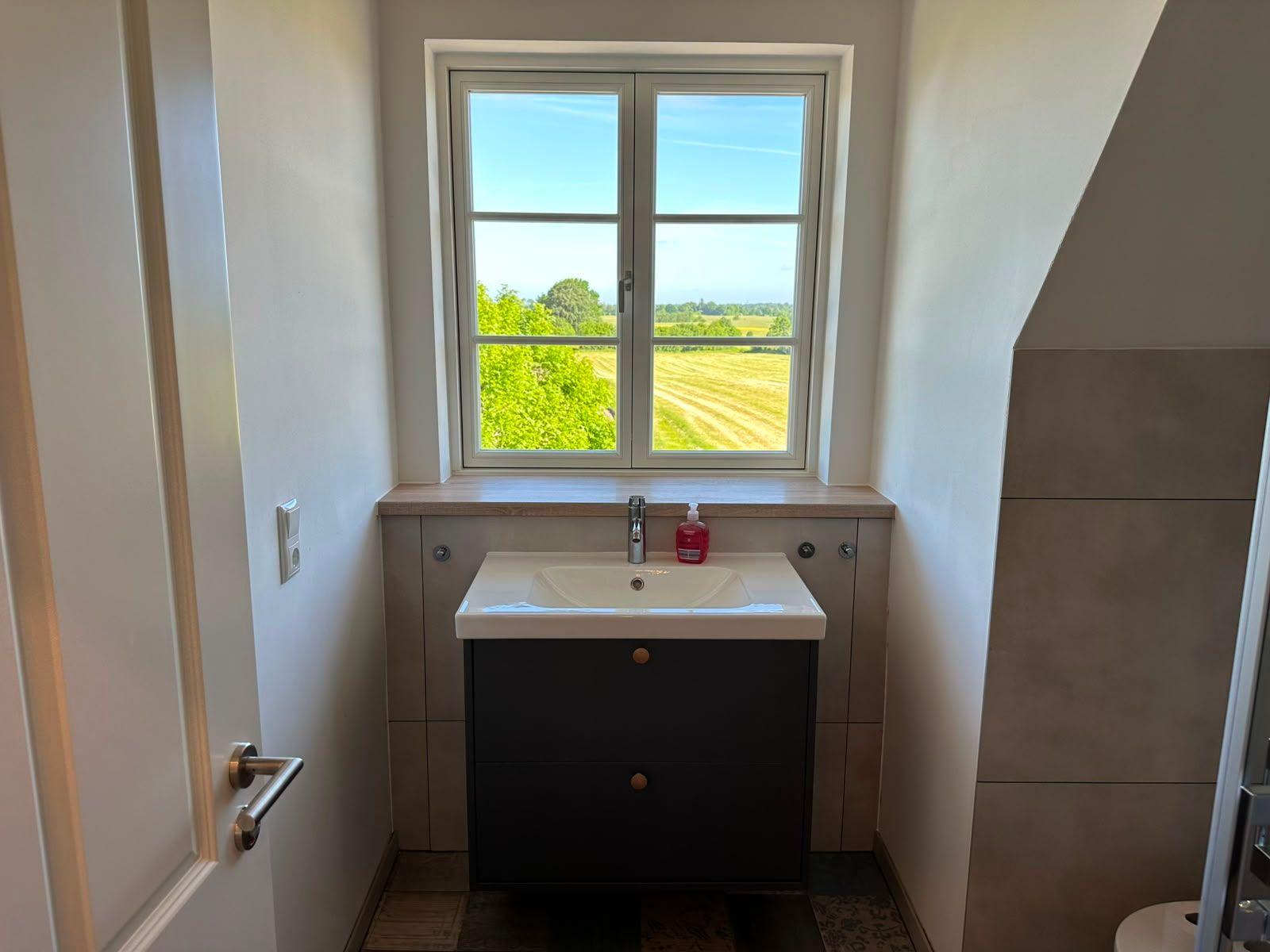 Badezimmer mit Waschbecken und Fensterblick auf Felder