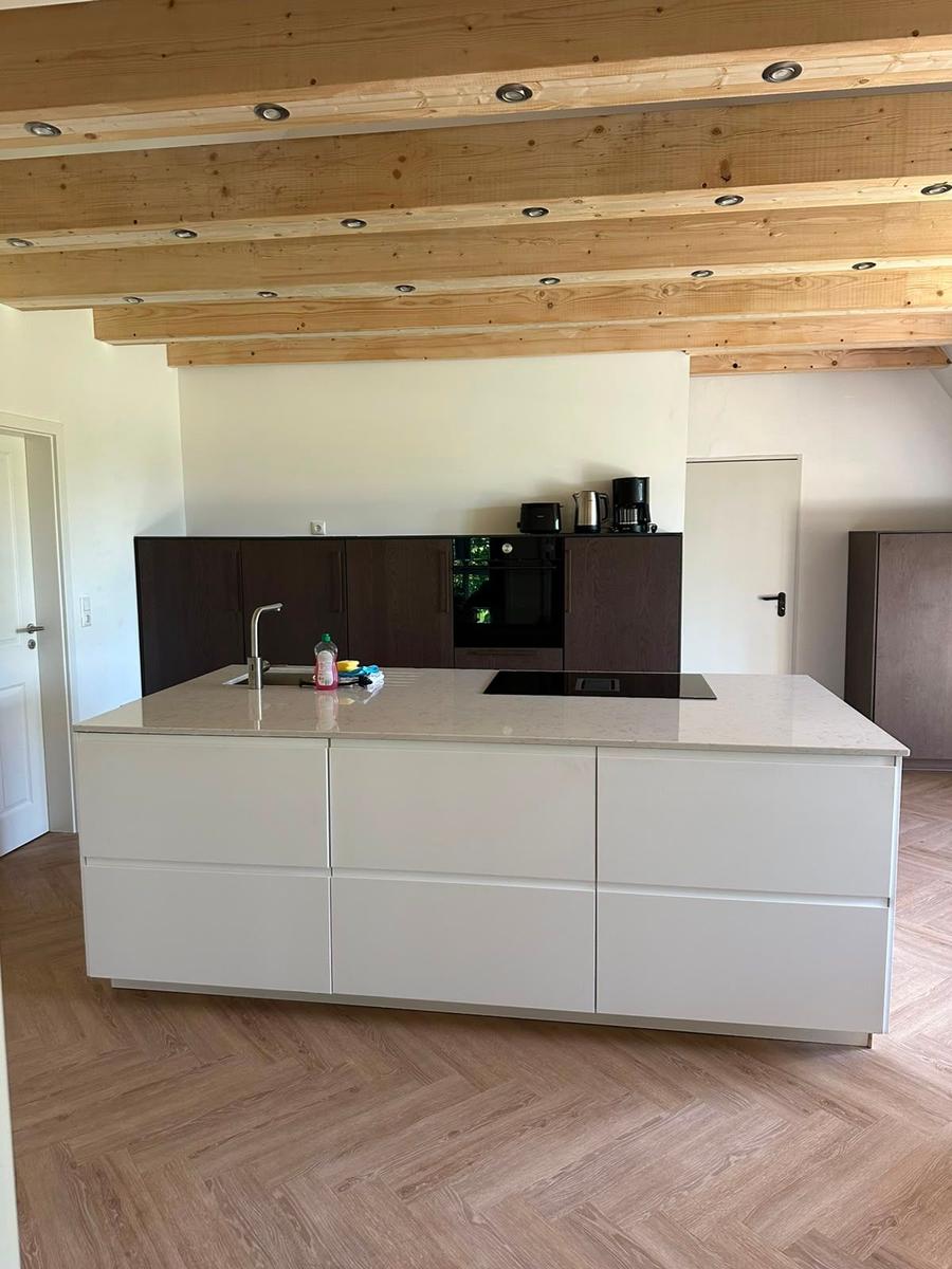 Moderne Küche mit Holzbalkendecke und hellen Arbeitsplatten.