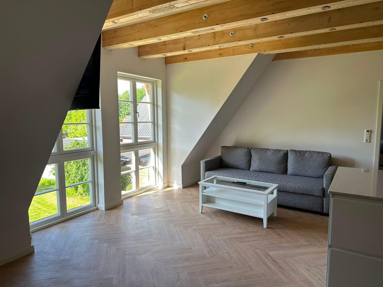 Wohnzimmer mit grauem Sofa, Glas-Tisch und Holzbalken an der Decke.