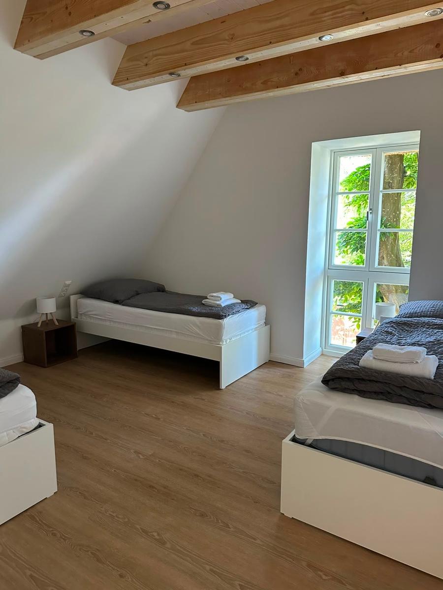 Zimmer mit zwei Betten, Holzbalken an der Decke und Fenster mit Blick auf Grün.