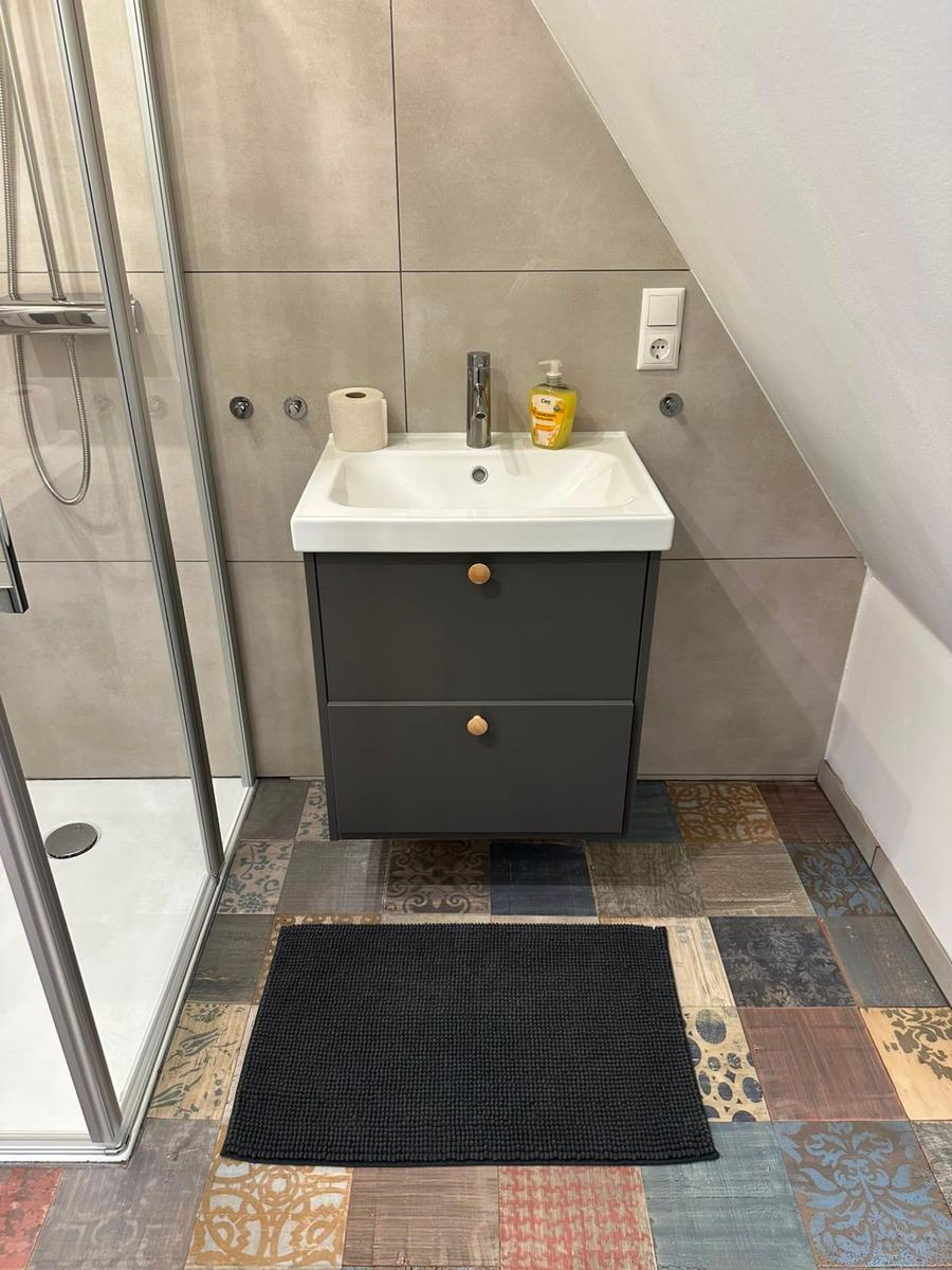 Badezimmer mit Waschbecken, Dusche und buntem Bodenfliesenmuster.