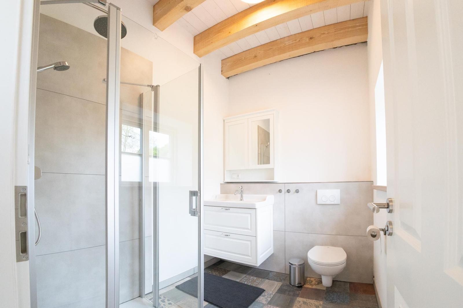 Badezimmer mit Dusche, Waschbecken und Toilette. Holzbalken an der Decke.