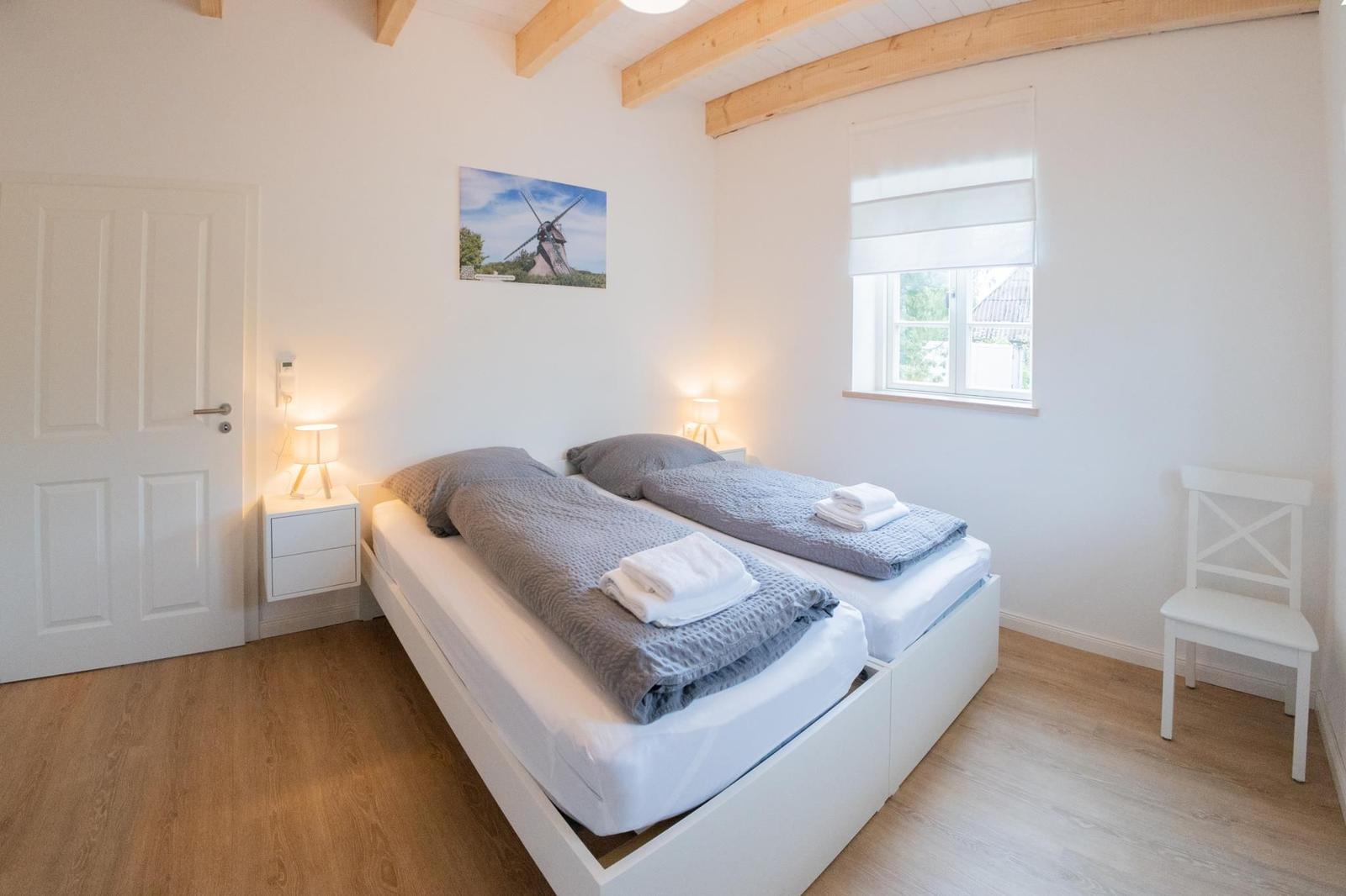 Zimmer mit Doppelbett, Fenster, Nachttisch und Stuhl. Holzdecke und Boden.