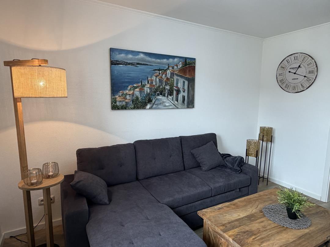Living room with gray sofa, wooden table, and wall art. A clock hangs on the wall.