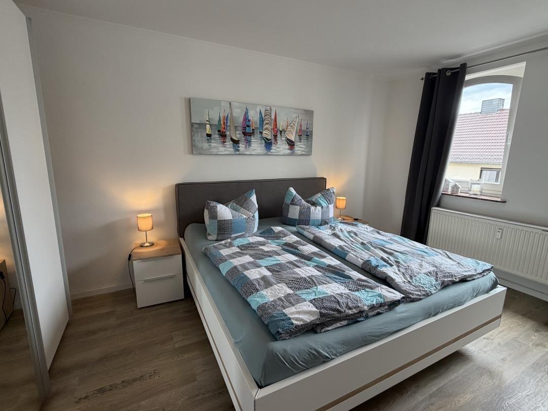 Bedroom with double bed, nightstands, and wall art with sailboats.