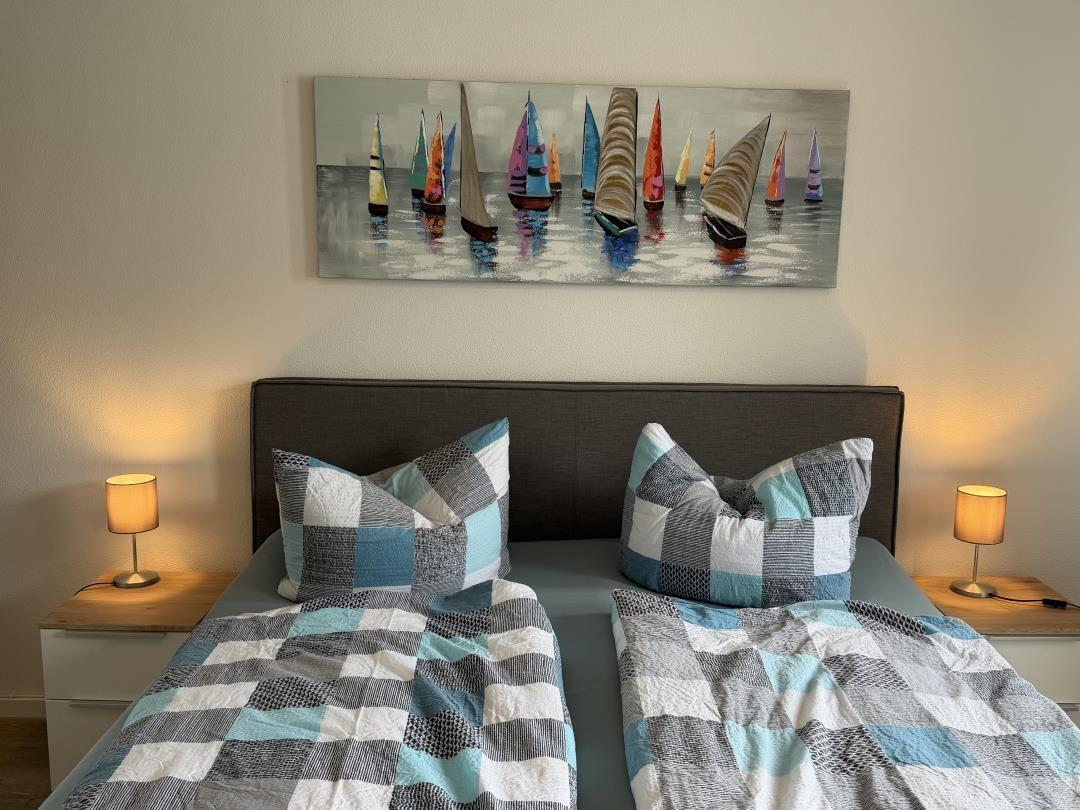 Double bed with patterned bedding and wall art of sailboats.