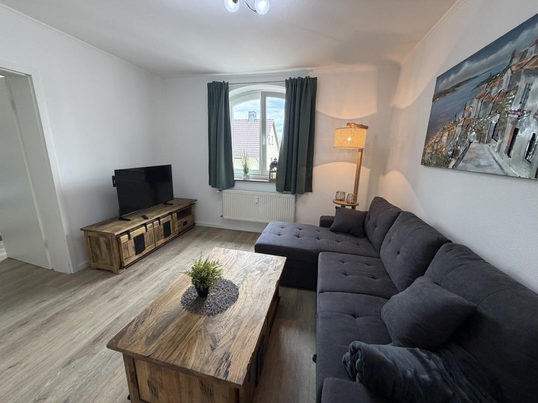 Living room with sofa, TV, and wooden table. Window with curtains and wall art.