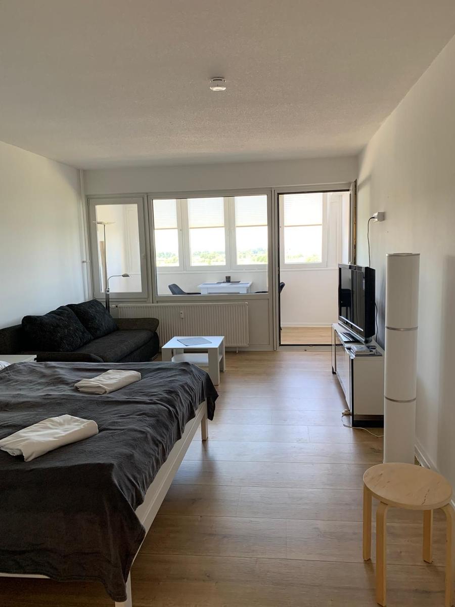 Schlafzimmer mit Bett, Sofa und TV. Holzboden und große Fenster.