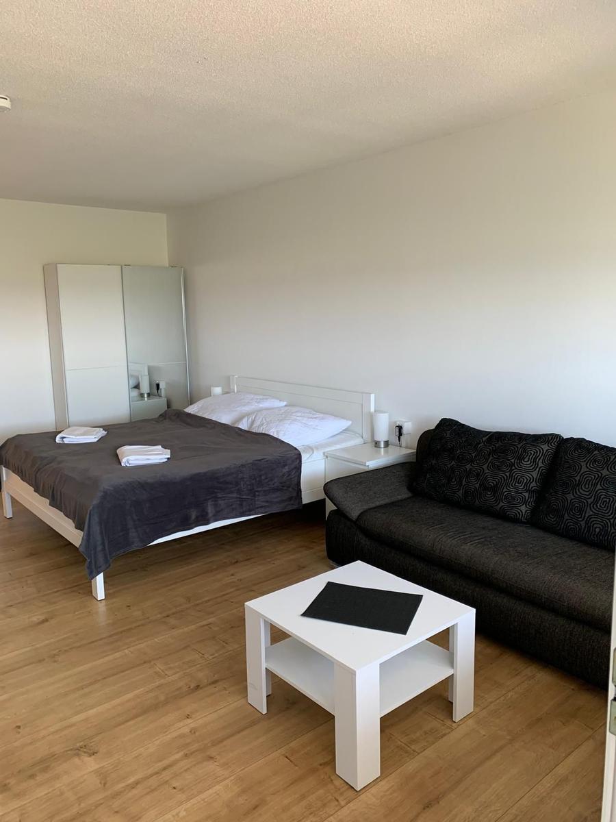 Schlafzimmer mit Bett, Sofa und Tisch. Holzboden und weiße Wände.