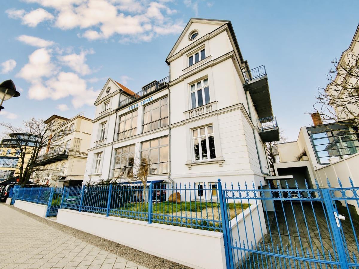 Weiße Villa mit blauem Zaun und Balkonen unter blauem Himmel.