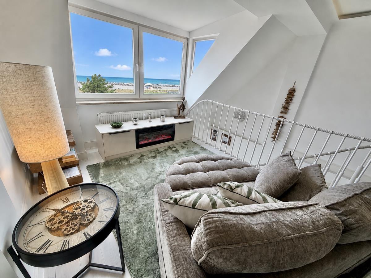 Wohnzimmer mit Blick auf Strand, Sofa, Kamin und Tisch mit Uhrmotiv.