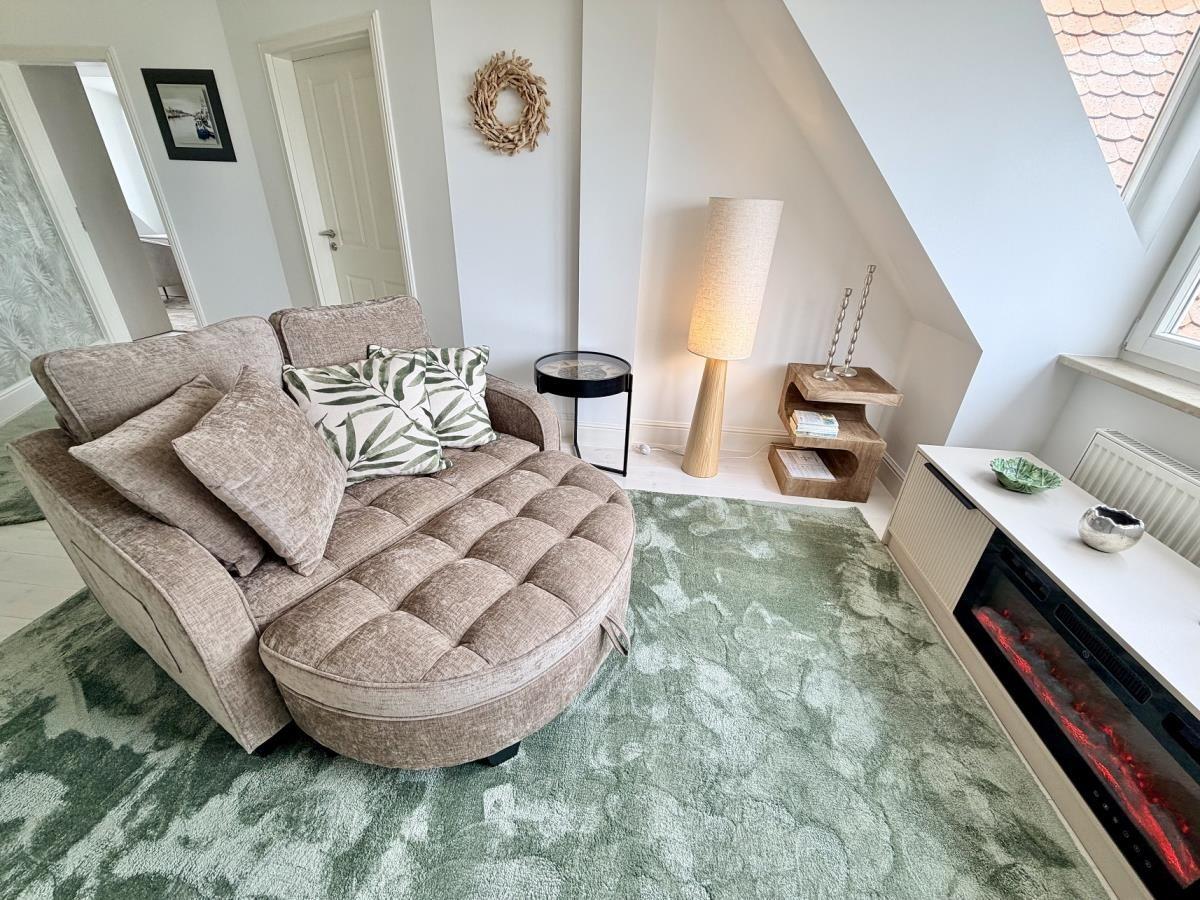 Ein Wohnzimmer mit Sofa, Teppich und Kamin. An der Wand hängt ein Kranz.