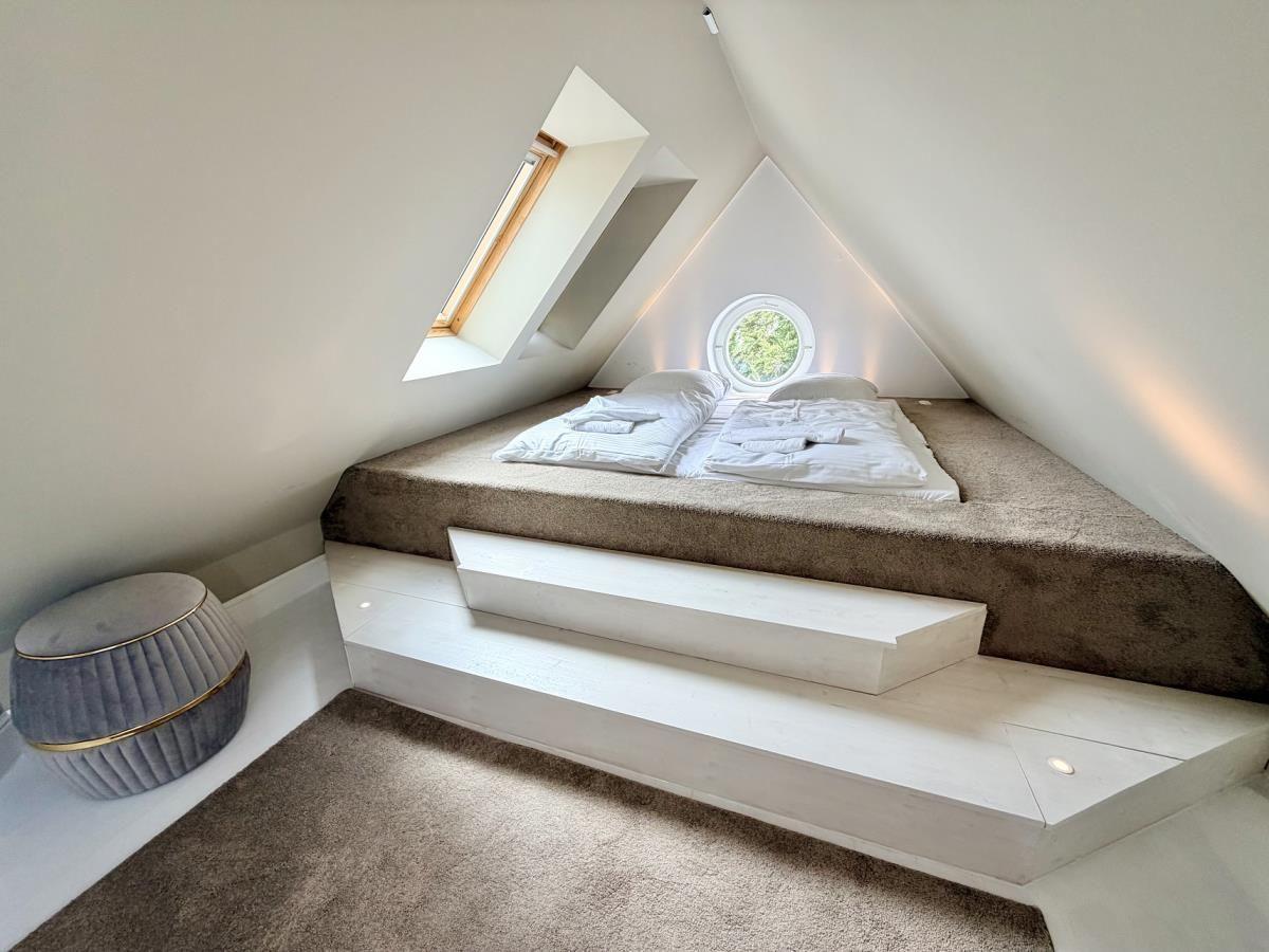 Ein Dachgeschosszimmer mit Bett, runden Fenster und Treppenstufen.