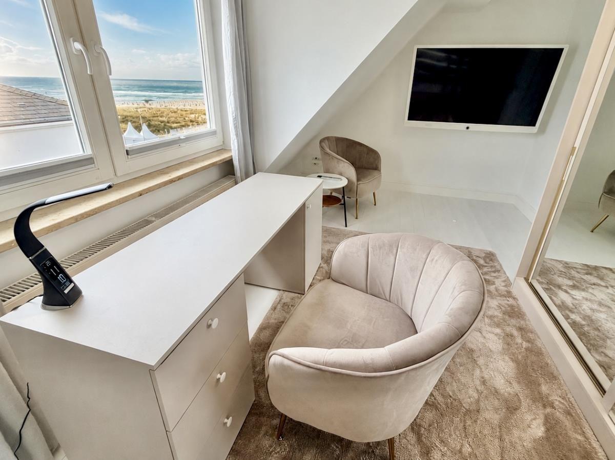Schlafzimmer mit Blick aufs Meer, Schreibtisch, Sessel und Wandfernseher.