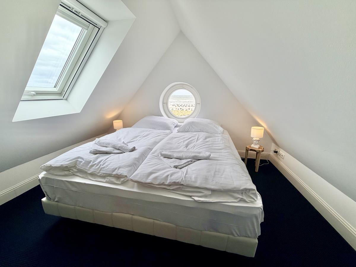 Schlafzimmer mit Doppelbett, runden Fenster und Dachfenster. Dunkler Teppich und zwei Nachttische.