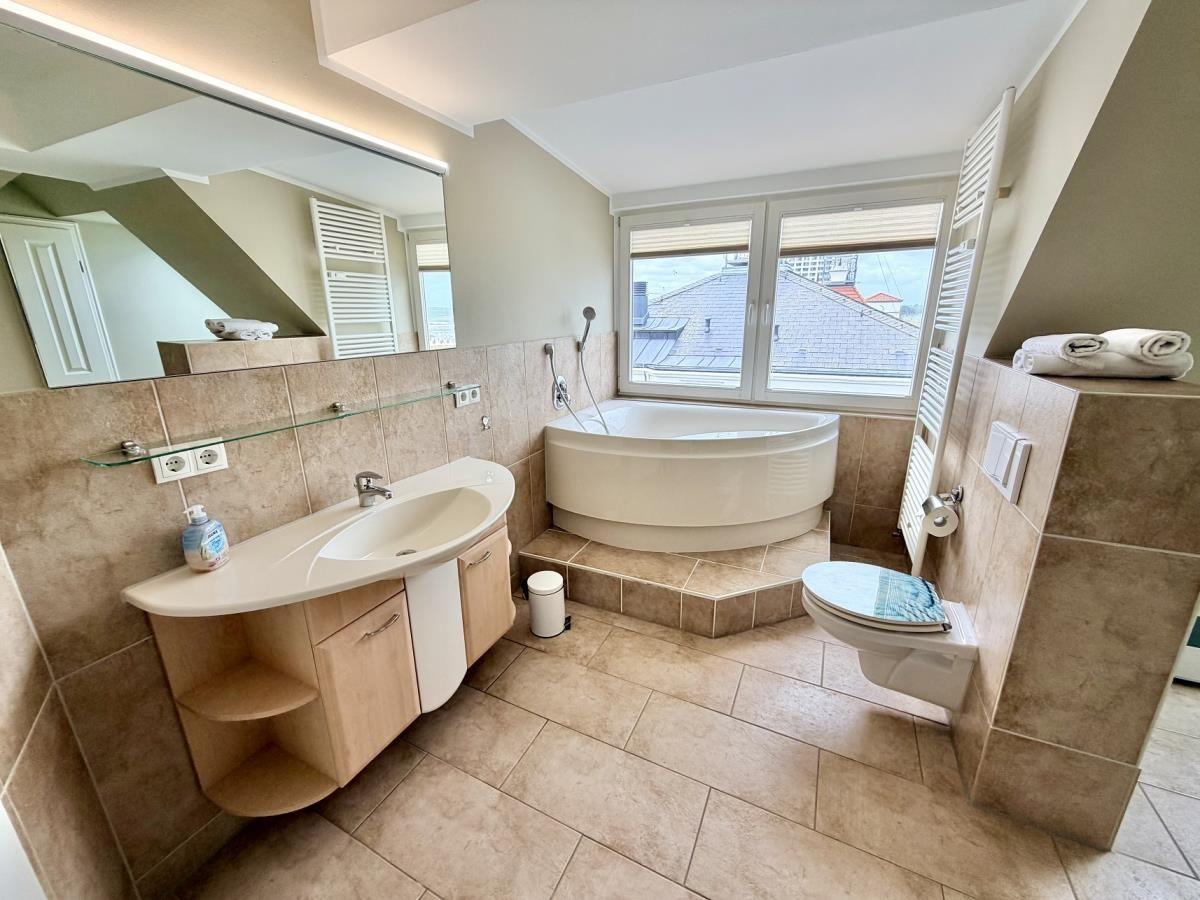 Badezimmer mit Badewanne, Waschbecken und Toilette. Fenster mit Blick auf Dächer.