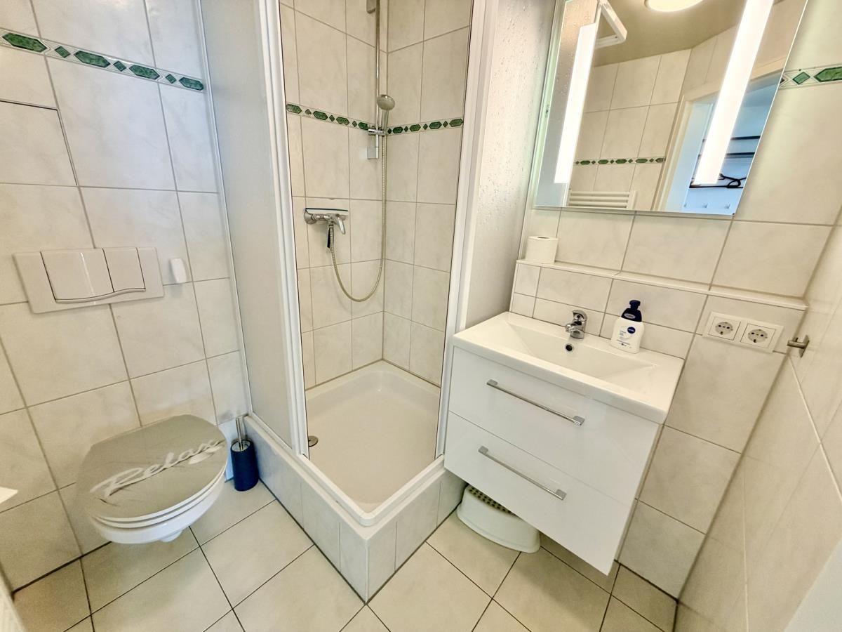 Badezimmer mit Dusche, Waschbecken und Toilette. Fliesenwand mit grüner Zierleiste.