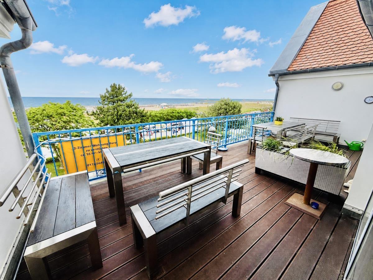 Terrasse mit Tisch, Bänken und Meerblick. Holzdielen, Metallgeländer, Pflanzen.