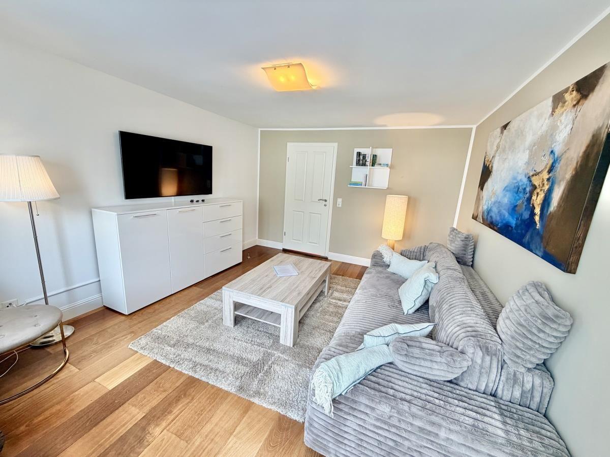 Wohnzimmer mit grauem Sofa, Fernseher und Holzboden.