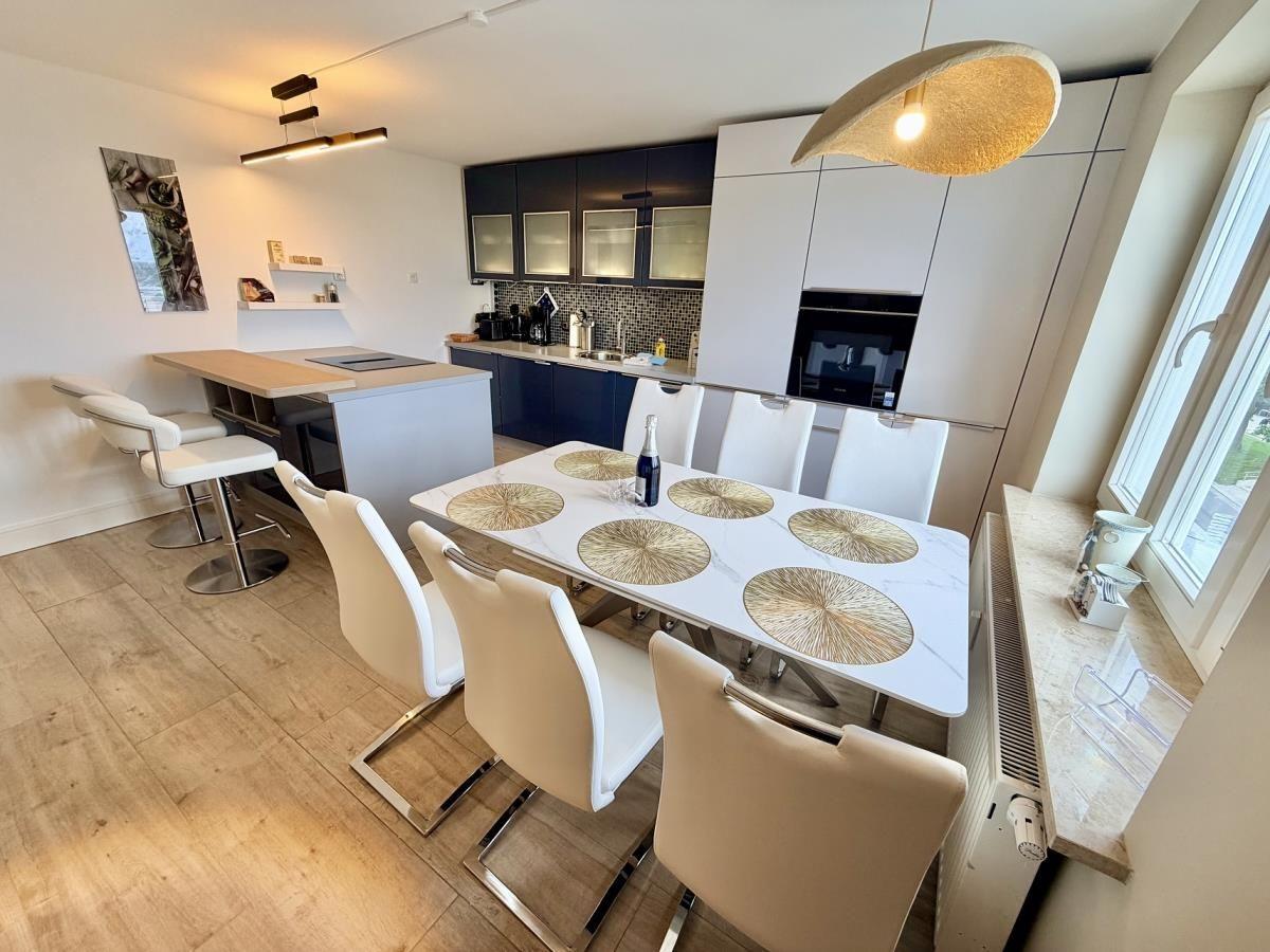 Moderne Küche mit Essbereich und Kücheninsel. Weiße Stühle um einen Tisch mit goldenen Untertassen.