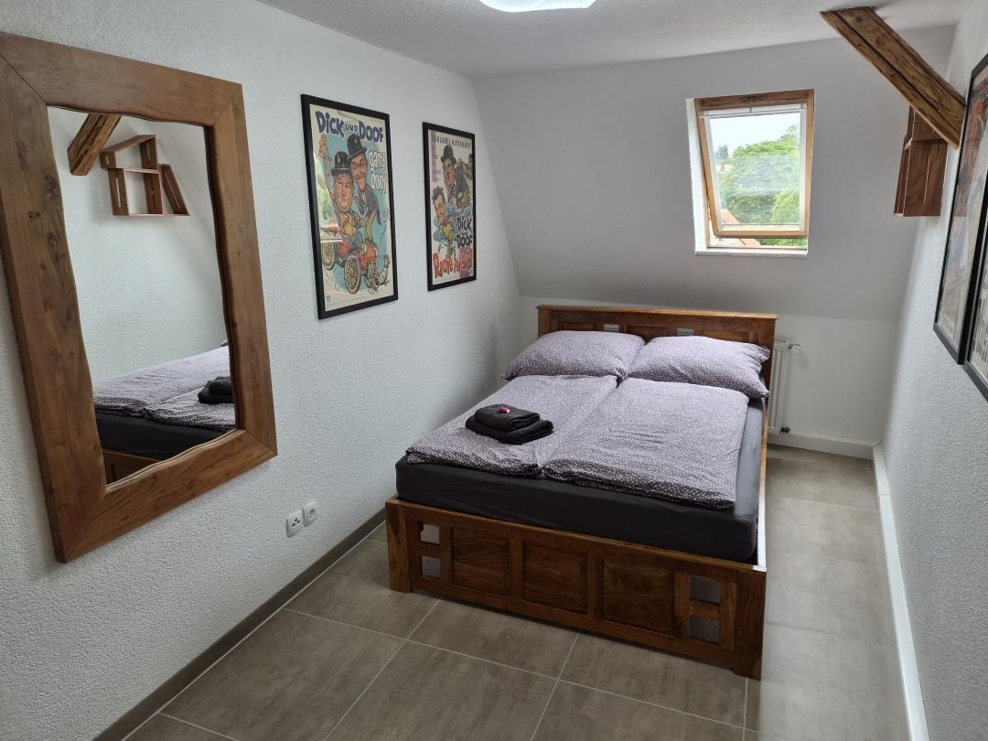 Bedroom with wooden bed, mirror, and window. Walls decorated with pictures.