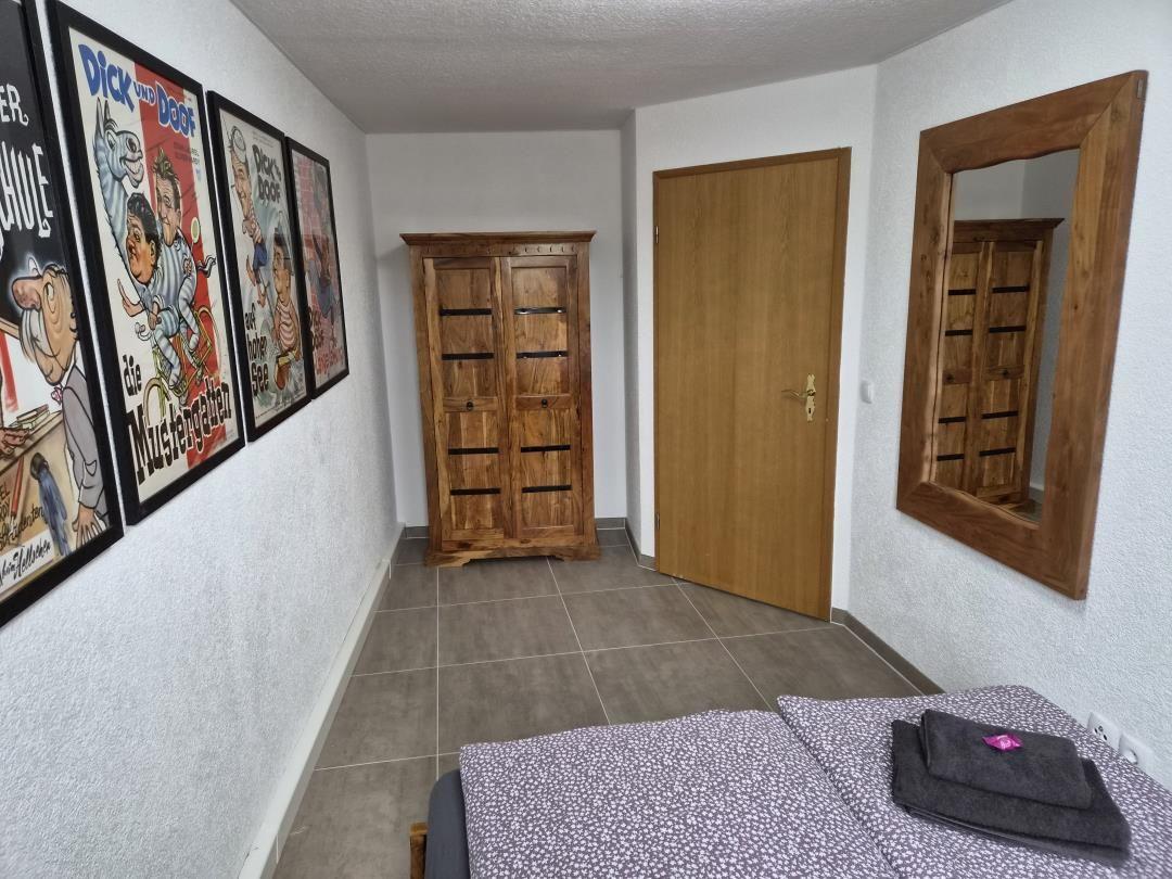 Bedroom with bed, wooden wardrobe, mirror, and wall posters.