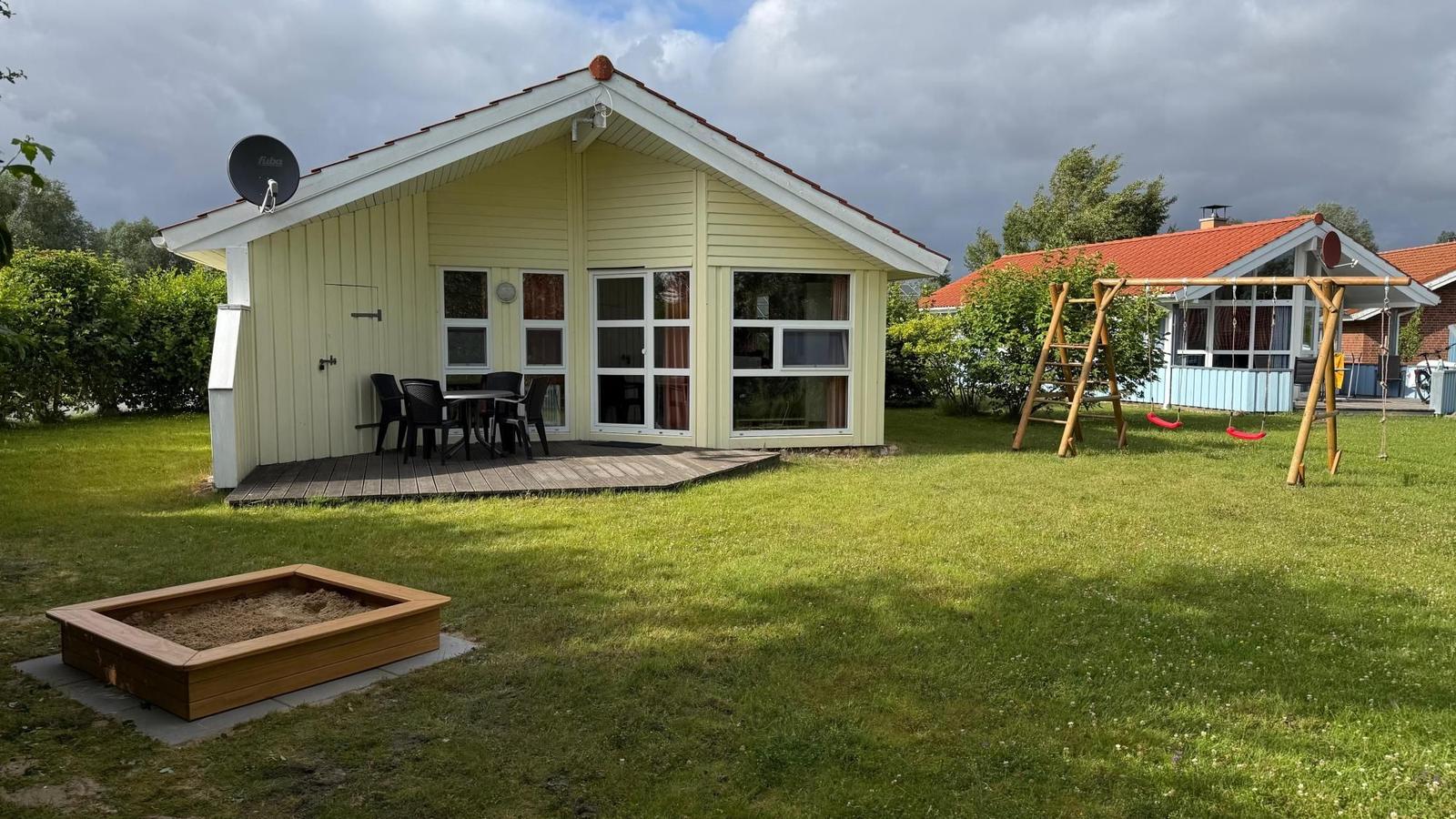 House with terrace, playground, and sandbox on green lawn.