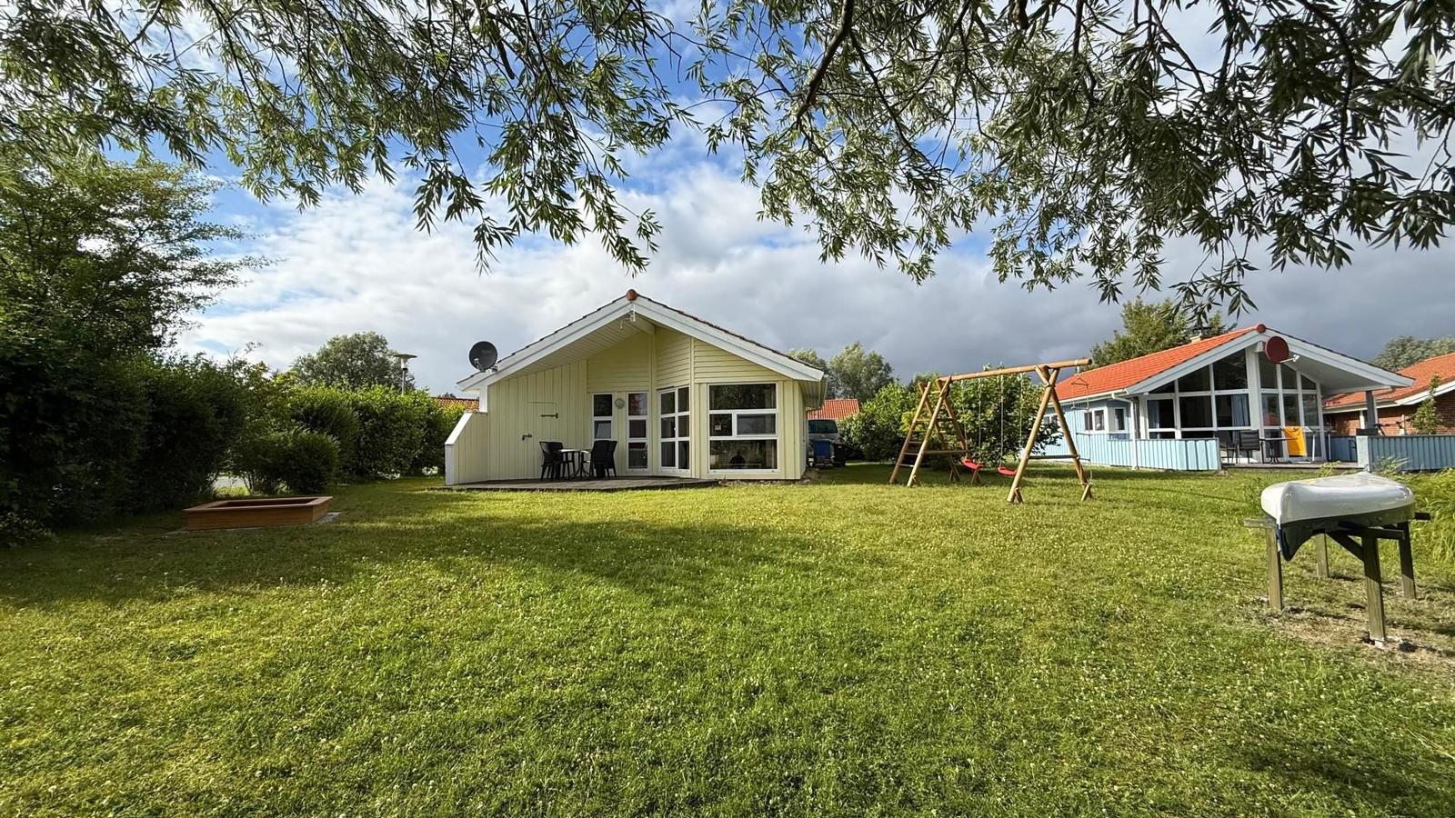 A yellow vacation house with terrace and playground in the grass. A boat is standing up.