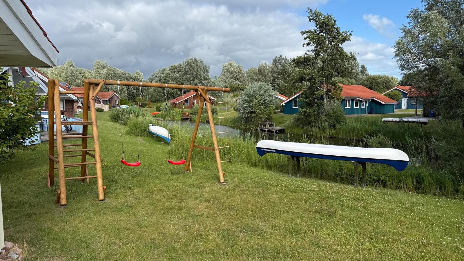 Behind the house is a playground with swings and climbing frame. Two canoes are on the lawn.