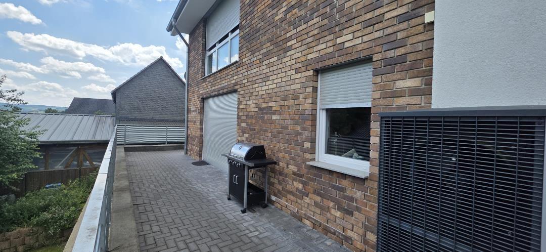 Terrasse mit Grill, braunem Backsteinhaus und Blick auf die Umgebung.