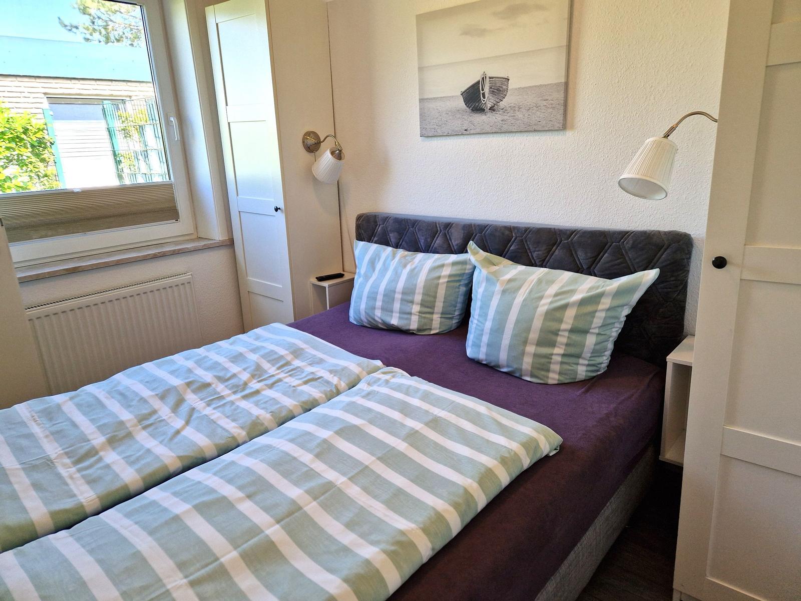 Schlafzimmer mit Doppelbett, Wandbild und zwei Nachttischen mit Lampen.