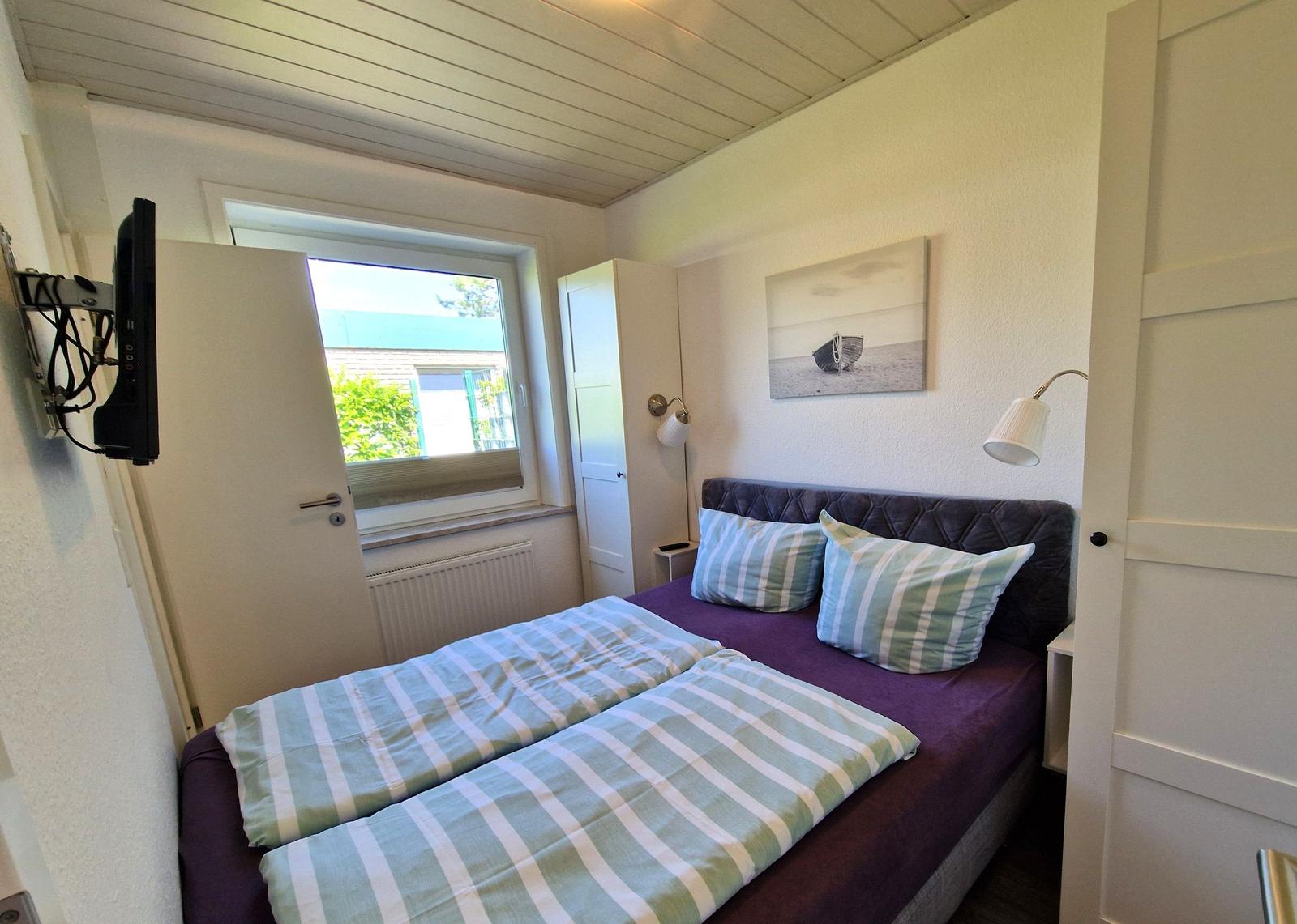 Schlafzimmer mit Doppelbett, Wandbild und Fenster. TV an der Wand montiert.