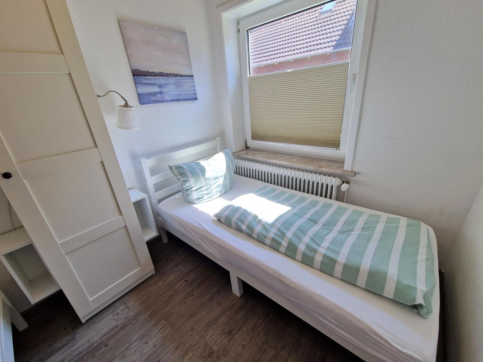 Ein Schlafzimmer mit einem Bett, einem Schrank und einem Fenster mit Jalousie.