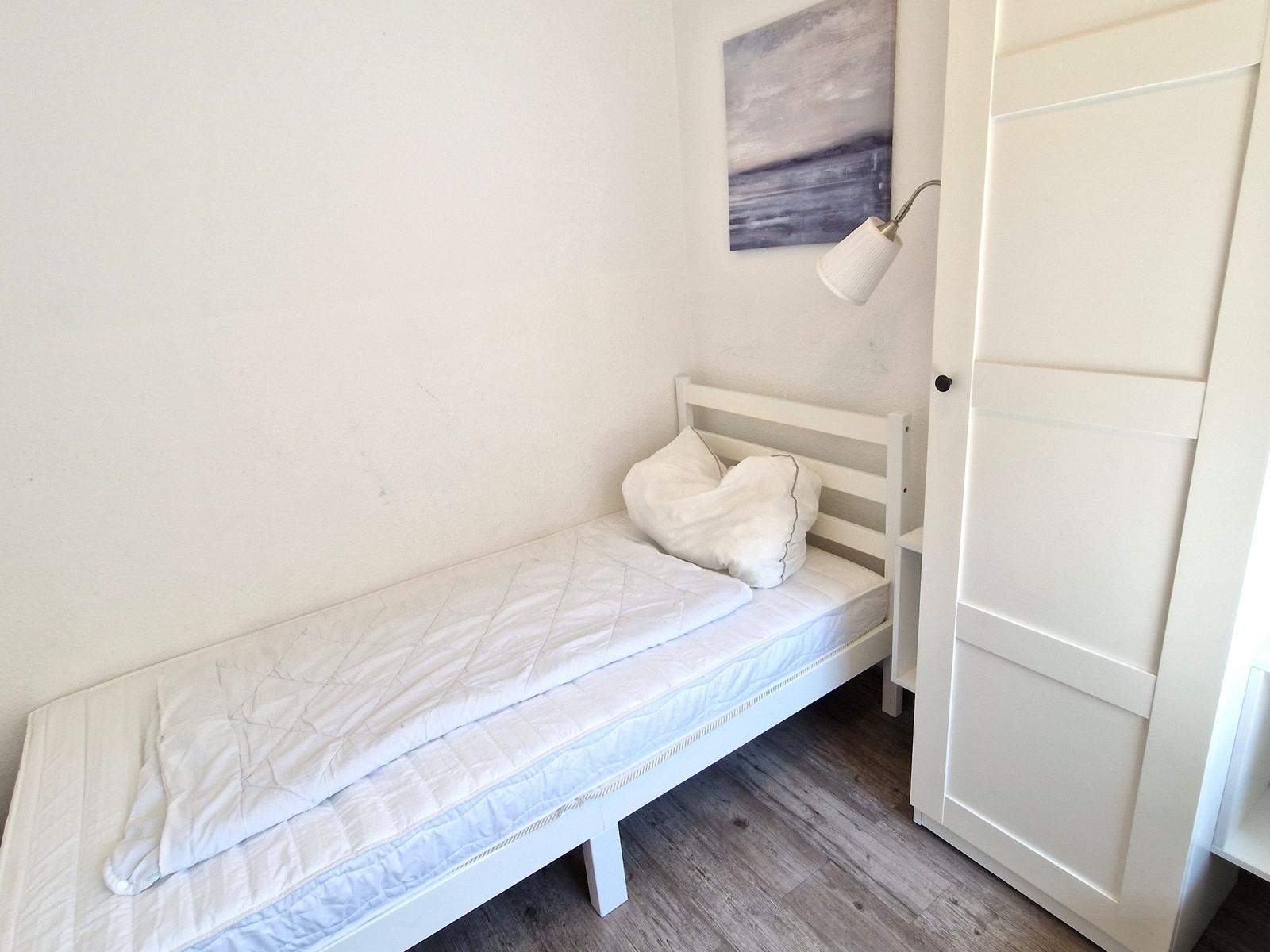 Ein Schlafzimmer mit weißem Bett, Wandbild und Schrank.