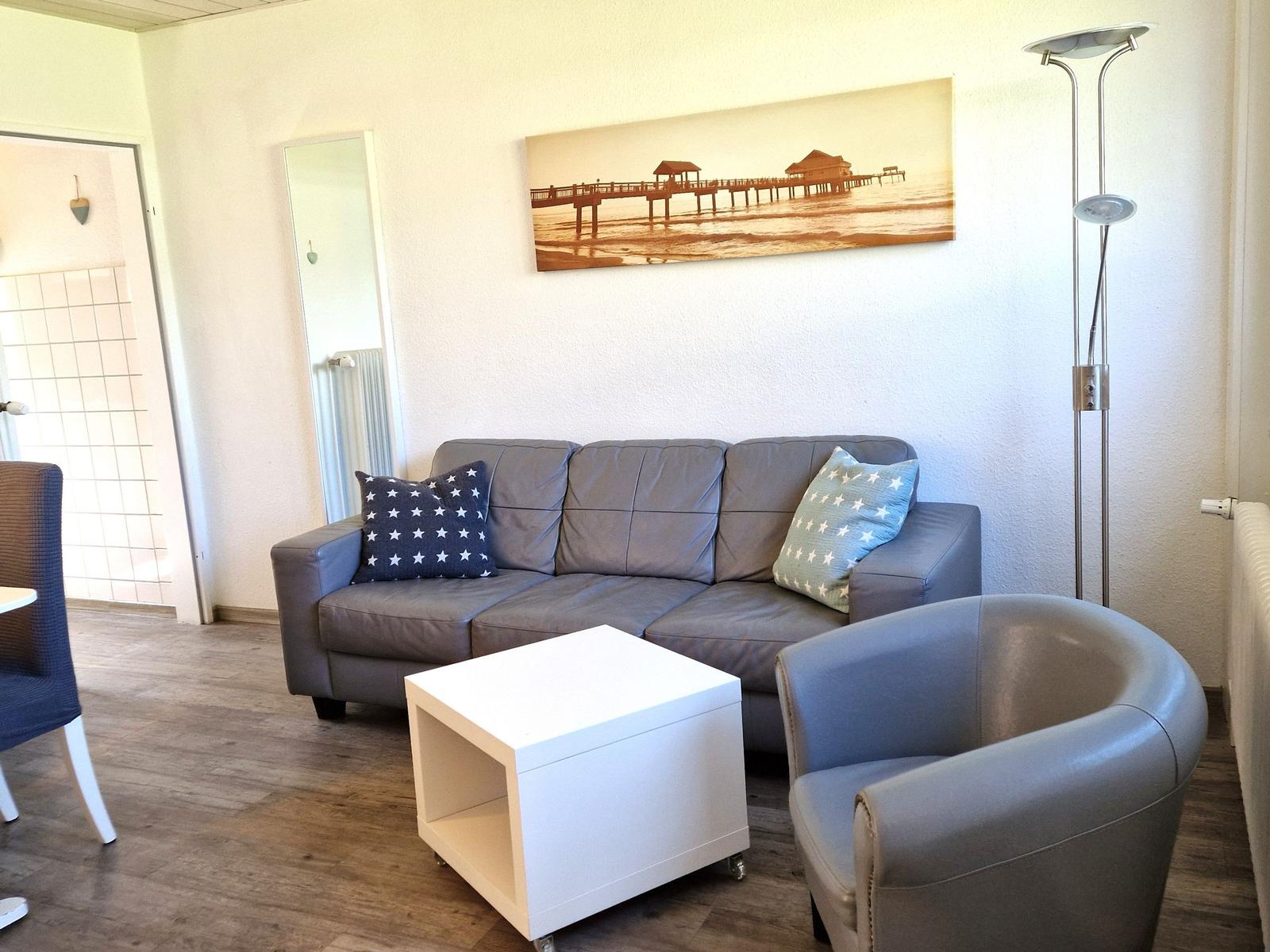 Ein Wohnzimmer mit grauem Sofa, Stuhl, weißem Tisch und Wandbild.