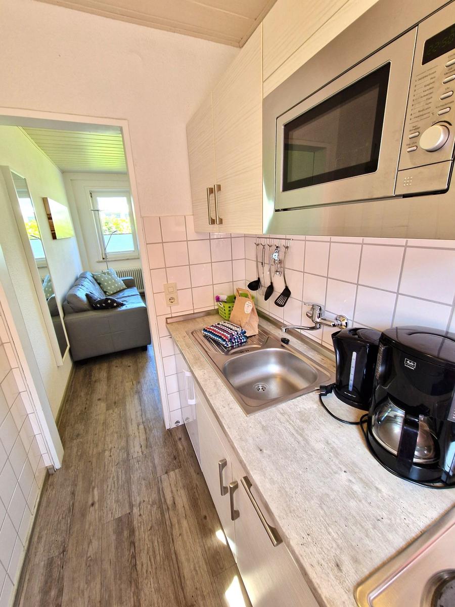 Küche mit Spüle, Mikrowelle und Kaffeemaschine. Wohnbereich mit Sofa im Hintergrund.