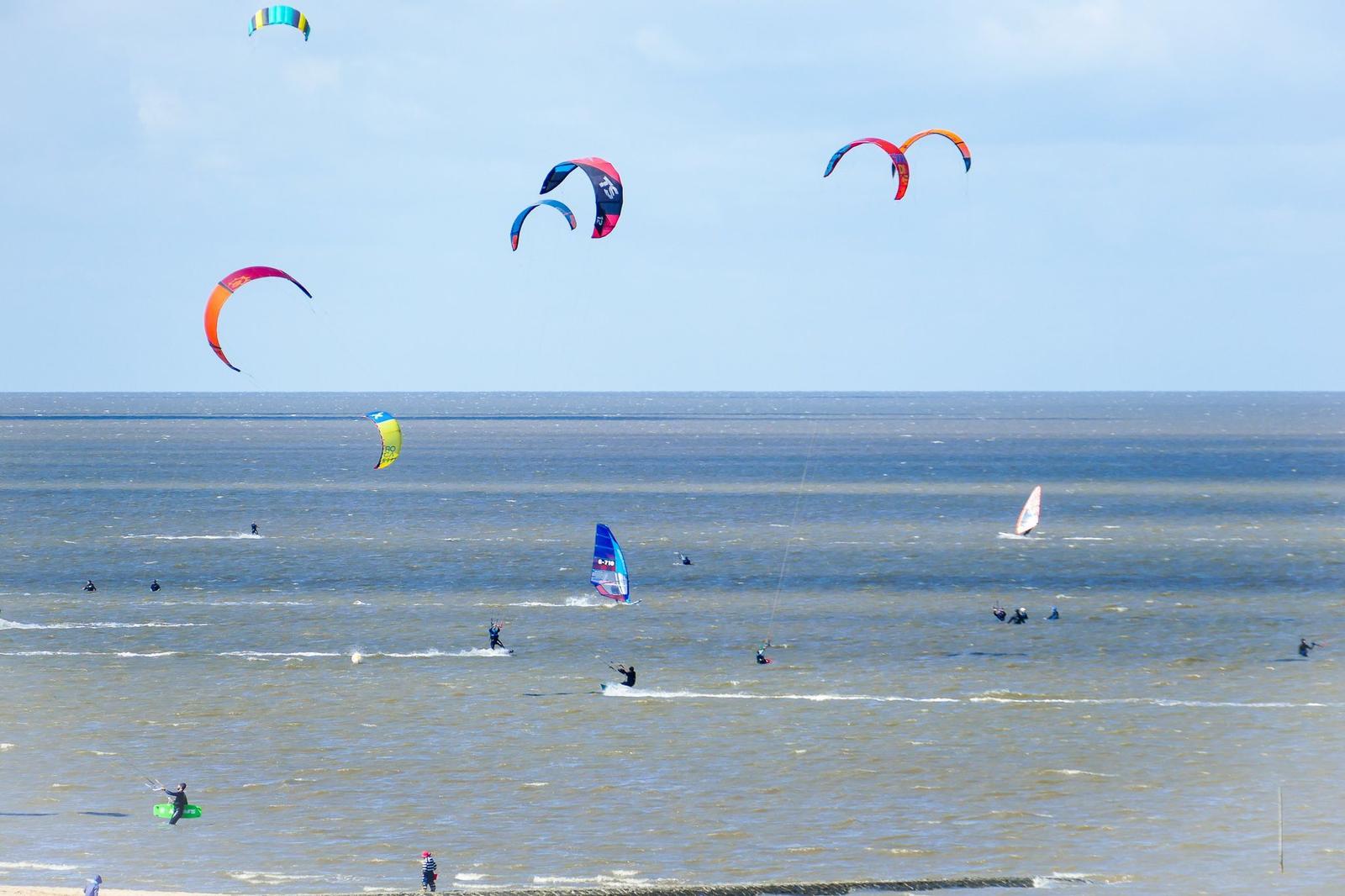 Mehrere Kitesurfer und Windsurfer auf dem Wasser mit bunten Kites am Himmel.
