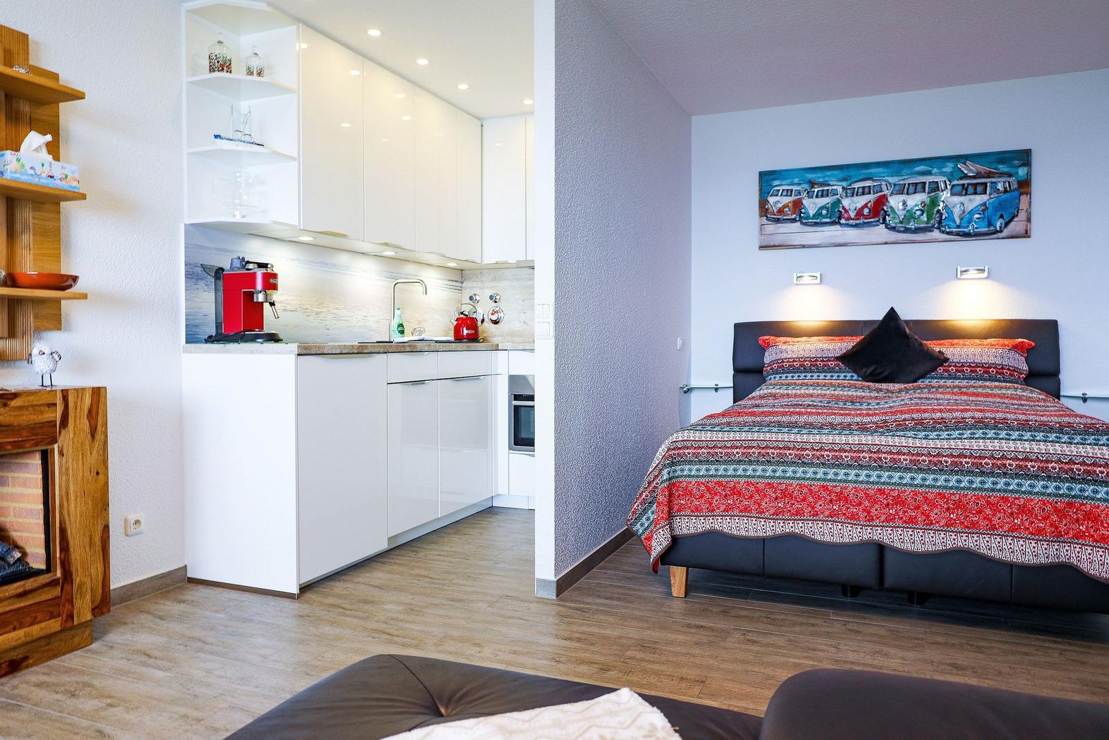 Schlafzimmer mit Bett und Wandbild. Küche mit Arbeitsplatte und Kaffeemaschine.