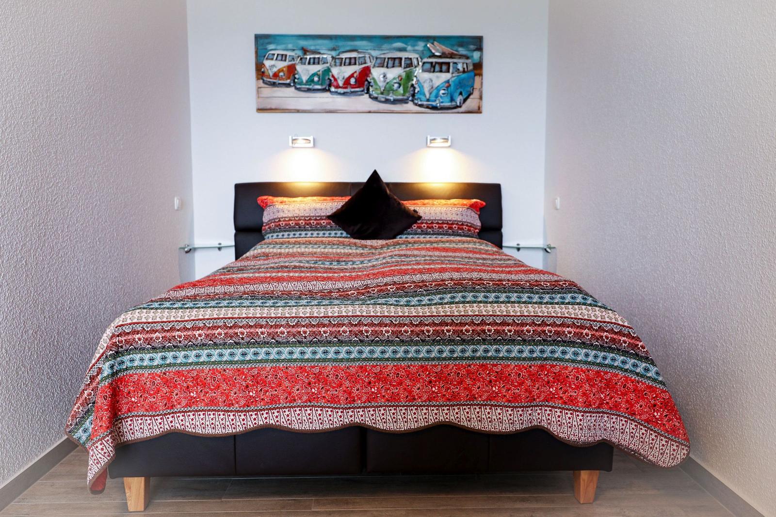 Schlafzimmer mit Bett, buntem Deckenbezug und Wandbild von VW-Bussen.