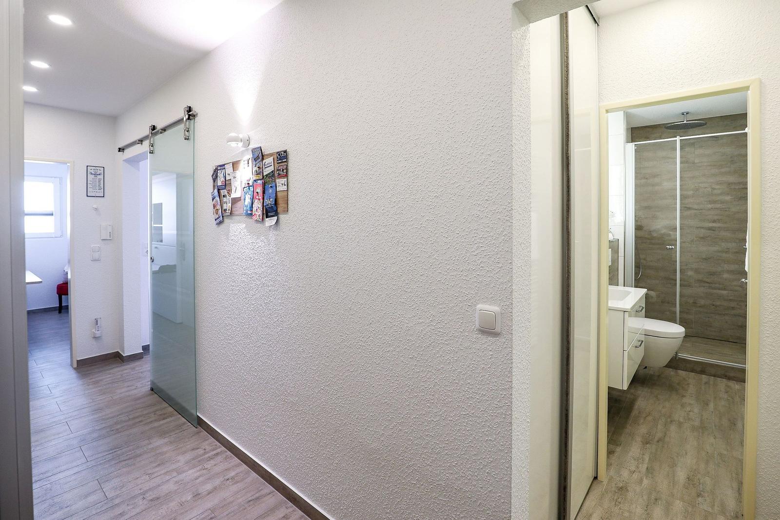 Flur mit Glaswand, Badezimmer und Blick in Wohnbereich.