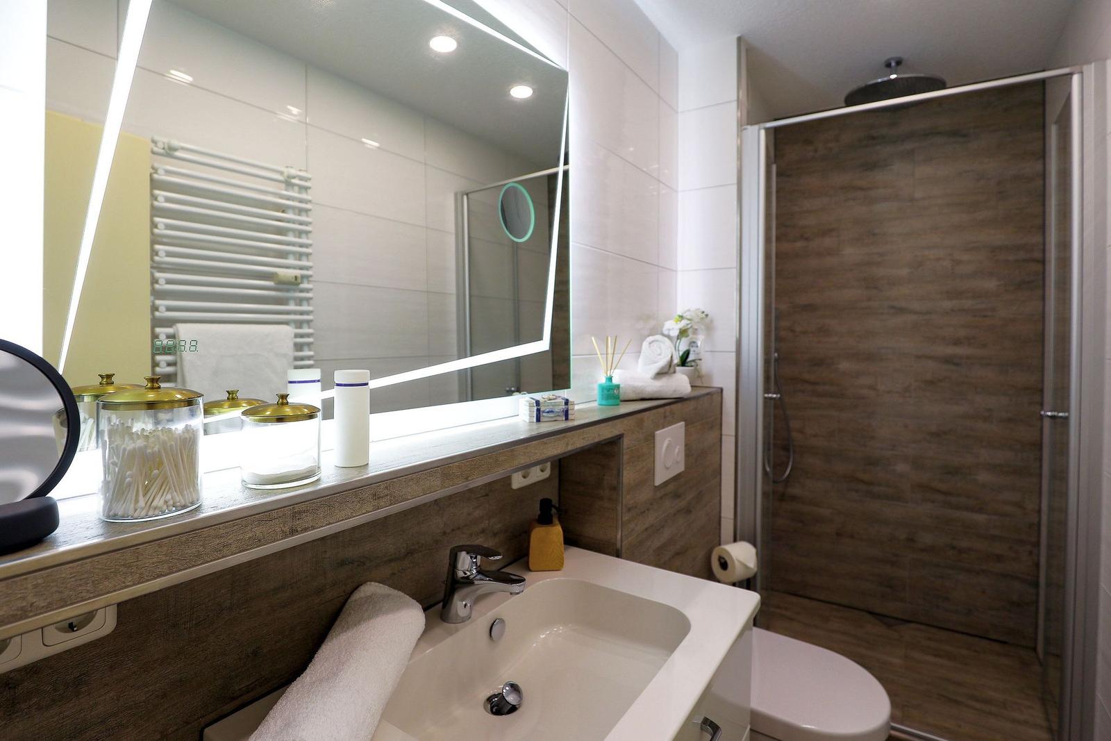 Bad mit Dusche, Waschbecken und beleuchtetem Spiegel.