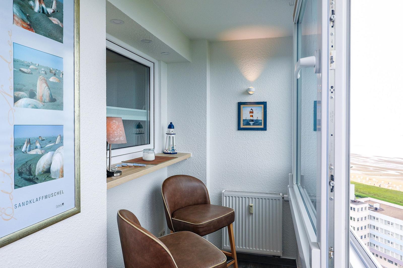 Balkon mit zwei braunen Stühlen, Tisch und Aussicht auf Strand und Gebäude.